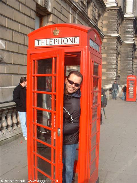 Smiling tourist in sunglasses inside a red London telephone booth