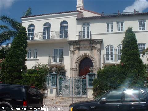 White Mediterranean-style mansion with carved stone entrance, cars parked in front