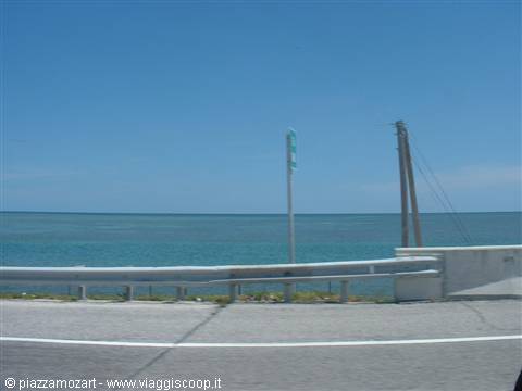 Coastal road with metal guardrail in front of turquoise sea under blue sky