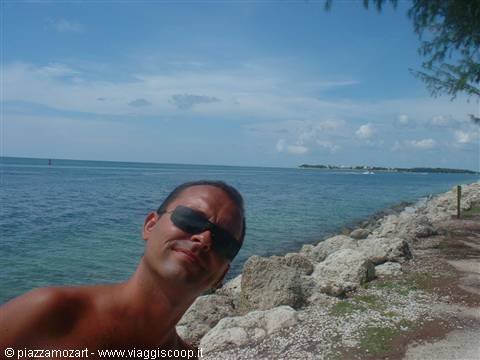 Man in sunglasses on rocky shore by turquoise sea and blue sky