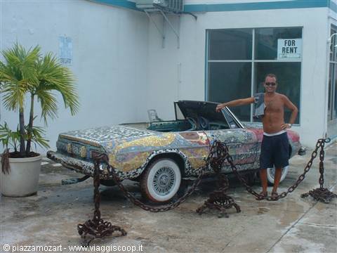 Man beside a mosaic-covered convertible car outside a shop with FOR RENT sign