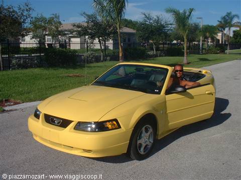 Smiling man driving a yellow Ford Mustang convertible under the sun
