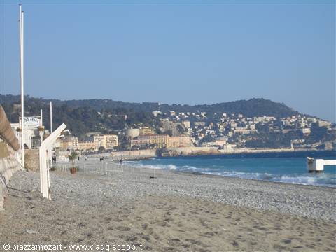 Pebble beach on Nice bay, colorful buildings below the hill