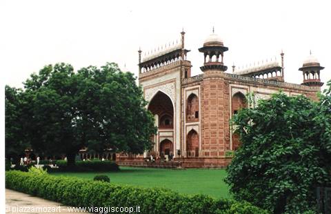 Red stone gateway with white domes and arches, green garden with visitors, Taj Mahal