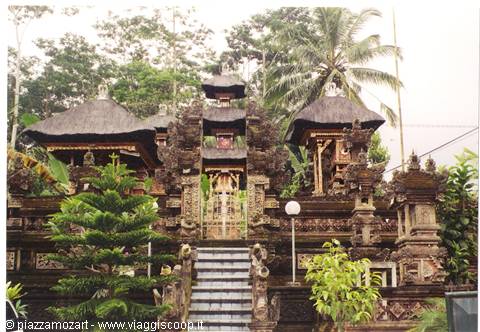Balinese temple with carved stone gates, thatched roofs and palm trees