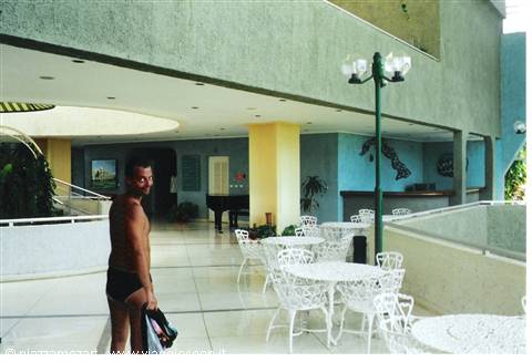Man in swim trunks beside white tables in hotel lobby