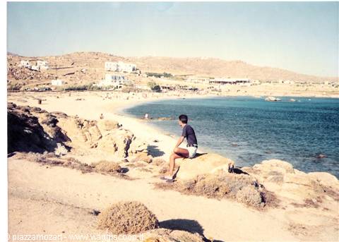 Boy sitting on a rock looks at the sandy beach and blue sea