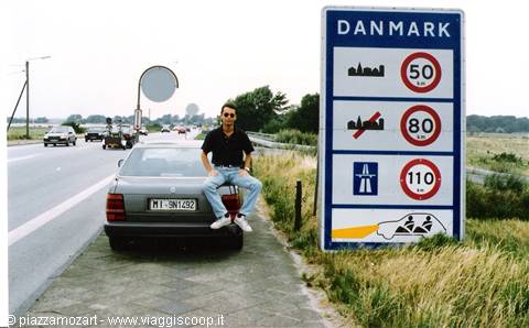 Young man sitting on a Mercedes hood beside the Denmark border sign