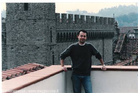 Man in sweater leaning on tiled terrace, crenellated walls of Bergamo Alta behind