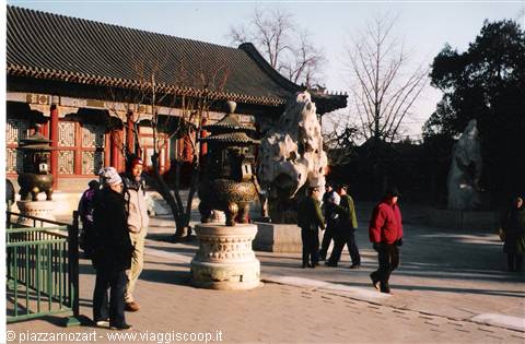 Tourists in Chinese temple courtyard with bronze incense burner and ornamental rocks