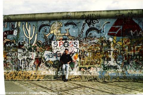 Man posing in front of graffiti-covered Berlin Wall, East Side Gallery