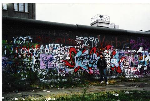 Berlin Wall covered in graffiti, man standing beneath a grey sky