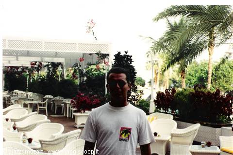 Man in sunglasses among wicker chairs and palm trees at an outdoor café