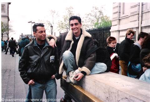 Two friends in leather jackets pose next to an iron gate