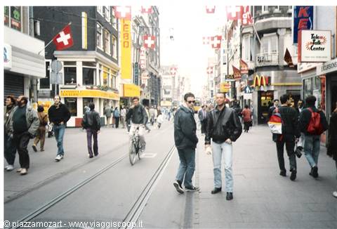 Pedestrians and cyclists on a shopping street with Swiss flags and storefronts