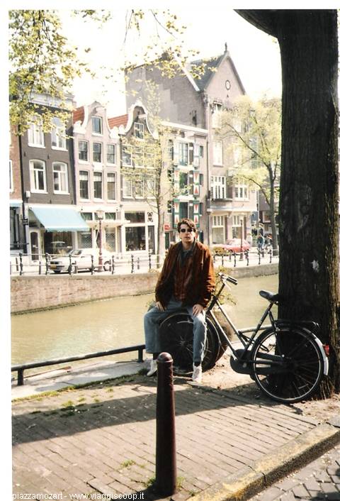Young man with brown jacket and bike beside an Amsterdam canal