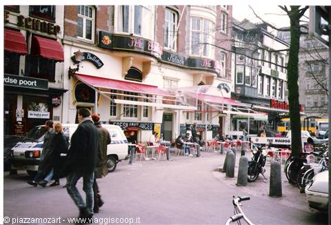 Pedestrians and bikes outside a café with red awnings, Amsterdam