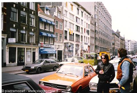 Two young men in leather talk between parked cars by Amsterdam canal houses