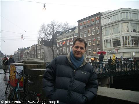 Man in puffer jacket and scarf on a bridge among Dutch houses and bicycles