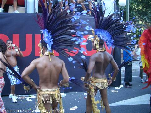 Two dancers with tall blue feather headdresses and golden skirts parade