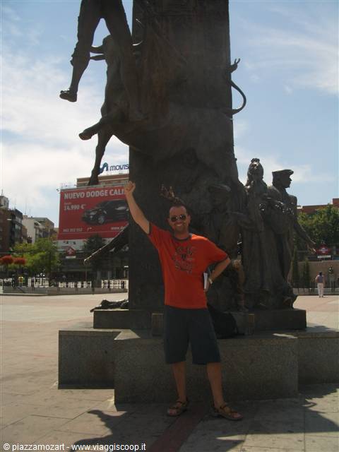 Tourist in red shirt poses under the bronze bull sculpture in Madrid
