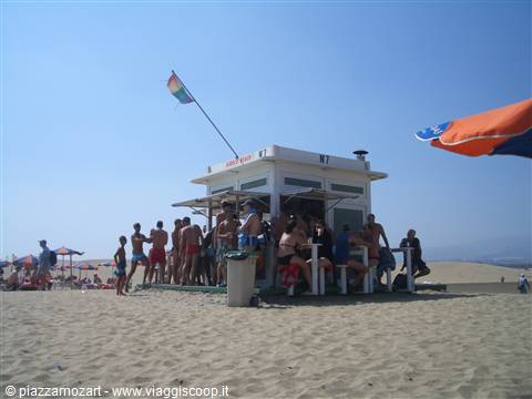 Wooden beach kiosk with flag, swimmers gathered around the bar counter