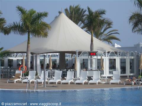 White loungers under tent by the pool with palm trees