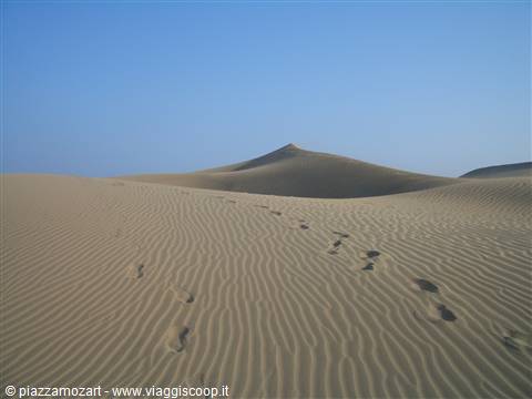Footprints across wind-rippled sand dunes under a clear sky