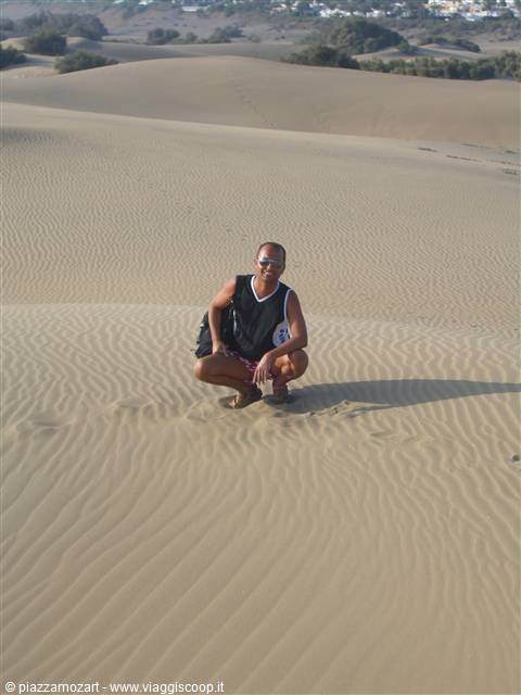Tourist crouching on the Maspalomas sand dunes, bright sunlight