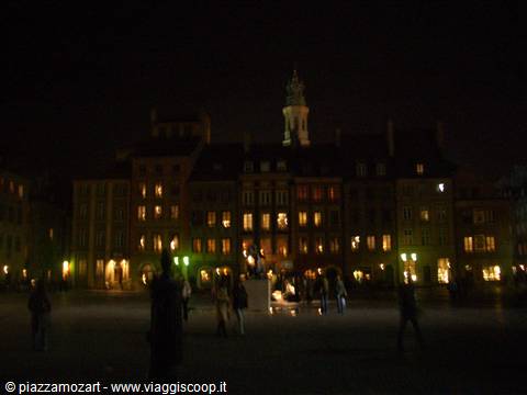 Warsaw Old Town square at night, lit historic buildings, people strolling about