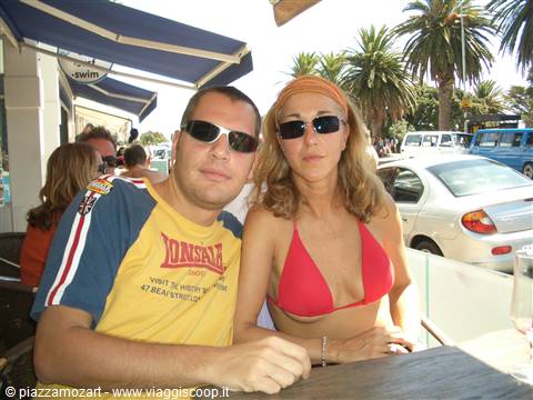 Couple in sunglasses sitting at an outdoor café table with palm trees