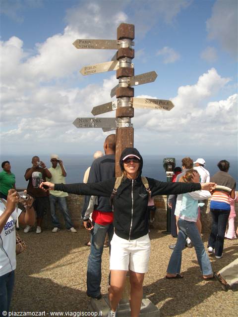 Woman with open arms beneath the Cape Point signpost, tourists and sea in the background