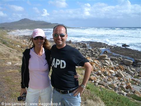 Couple in sunglasses on rocky beach, waves and hills behind