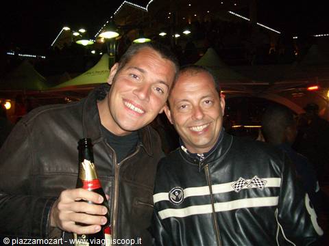 Two smiling friends with a beer bottle under festival night lights