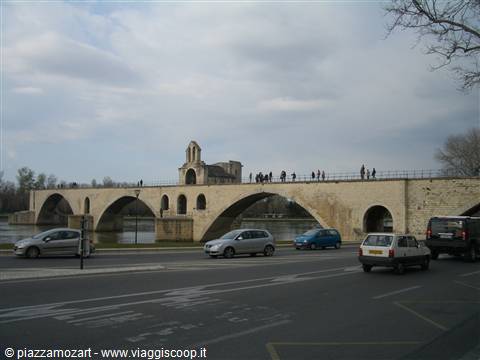 Tourists walk across the Saint-Bénézet bridge in Avignon, cars pass on the road below