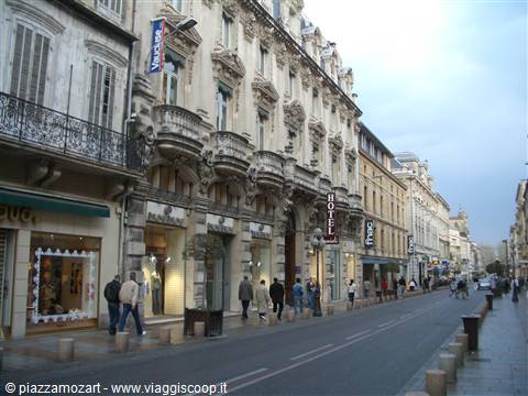 Pedestrians along a street with ornate stone buildings and hotel signs, Montpellier