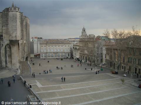 People stroll across the square by the Popes' Palace in Avignon under cloudy skies