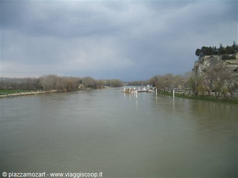 Boat moored on a muddy river, rocky cliff with trees under cloudy sky
