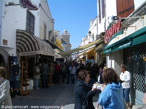Shoppers stroll a busy pedestrian street with striped awnings and shops