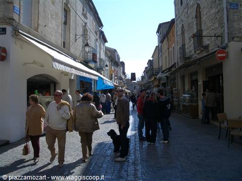 Tourists and a dog stroll past shops on a cobbled stone street