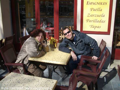 Smiling couple at an outdoor Spanish restaurant table with paella and tapas menu