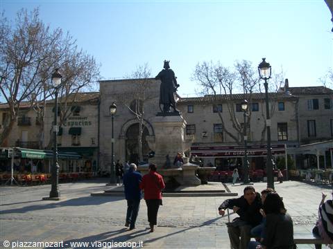 Statue on a fountain in a sunny square, people sitting at café tables