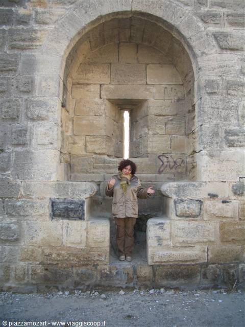 Woman in beige jacket under a large stone archway with a narrow bright slit