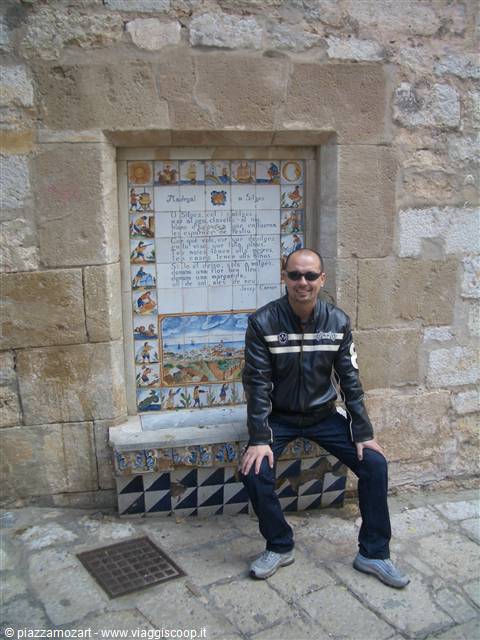 Man sitting beside a recipe painted on ceramic tiles, ancient stone wall
