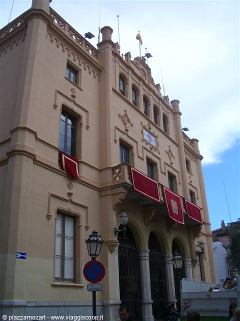 Ochre building with arches and red banners under a cloudy sky