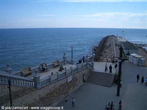Stone staircase with people and benches overlooking the sea, breakwater pier