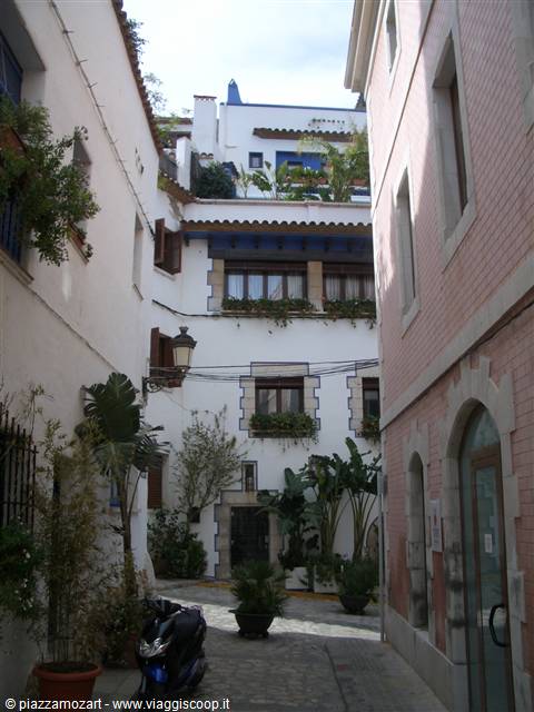 Alley between white and pink houses with potted plants and parked scooter