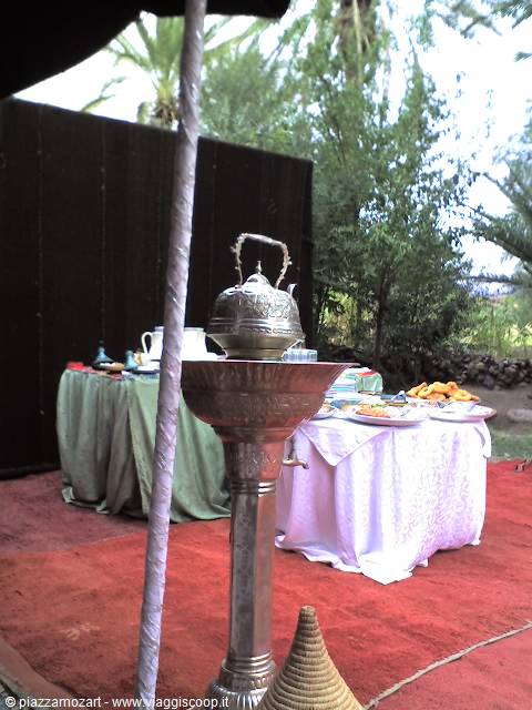 Silver teapot on a brazier, laden table under a tent among palms