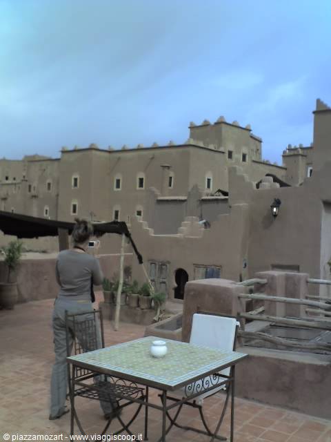 Woman photographs mud-brick kasbah buildings from a tiled terrace
