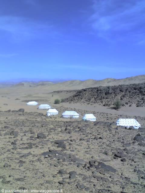 White tents of a desert camp among rocks and sand under blue sky